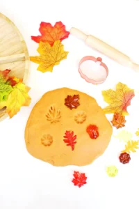 orange playdough with plastic leaves and pumpkins in it