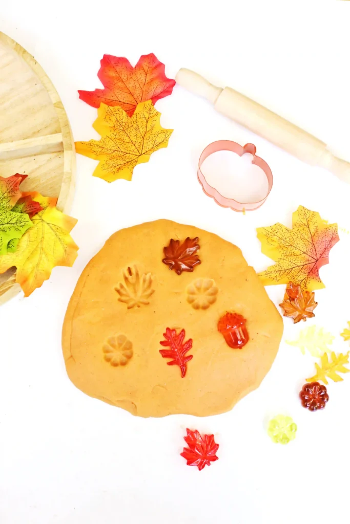 orange playdough with plastic leaves and pumpkins in it