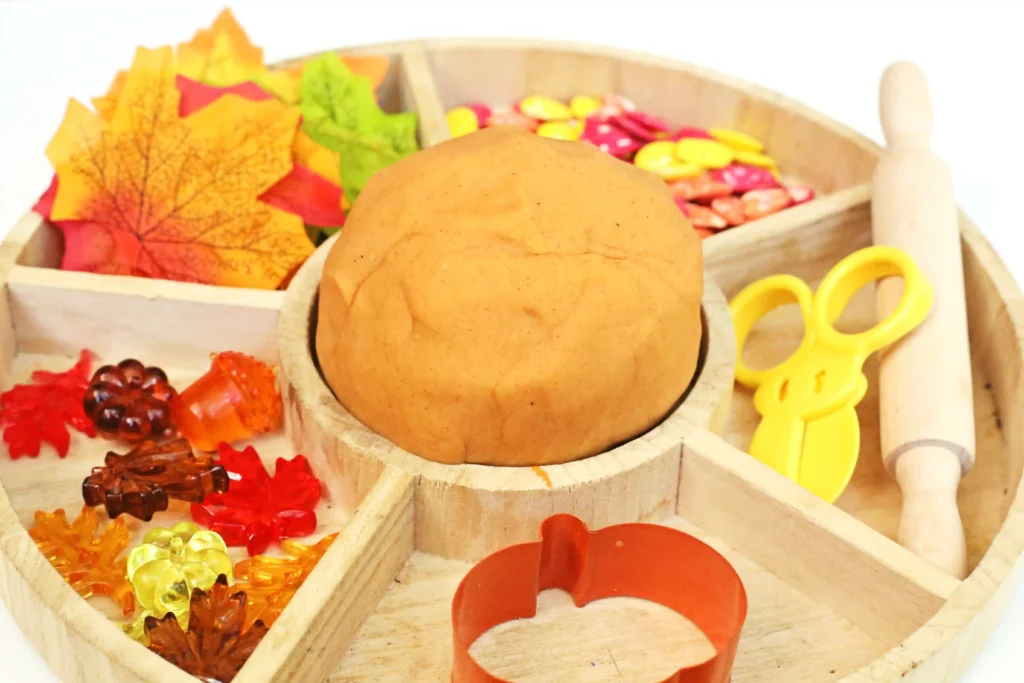a pumpkin playdough tray with pumpkin playdough, fake leaves and fake pumpkins