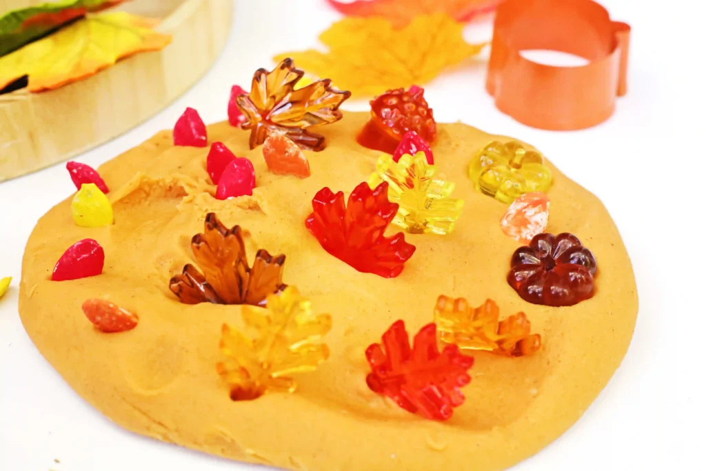 orange playdough with plastic leaves and pumpkins in it