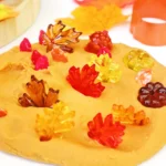 orange playdough with plastic leaves and pumpkins in it