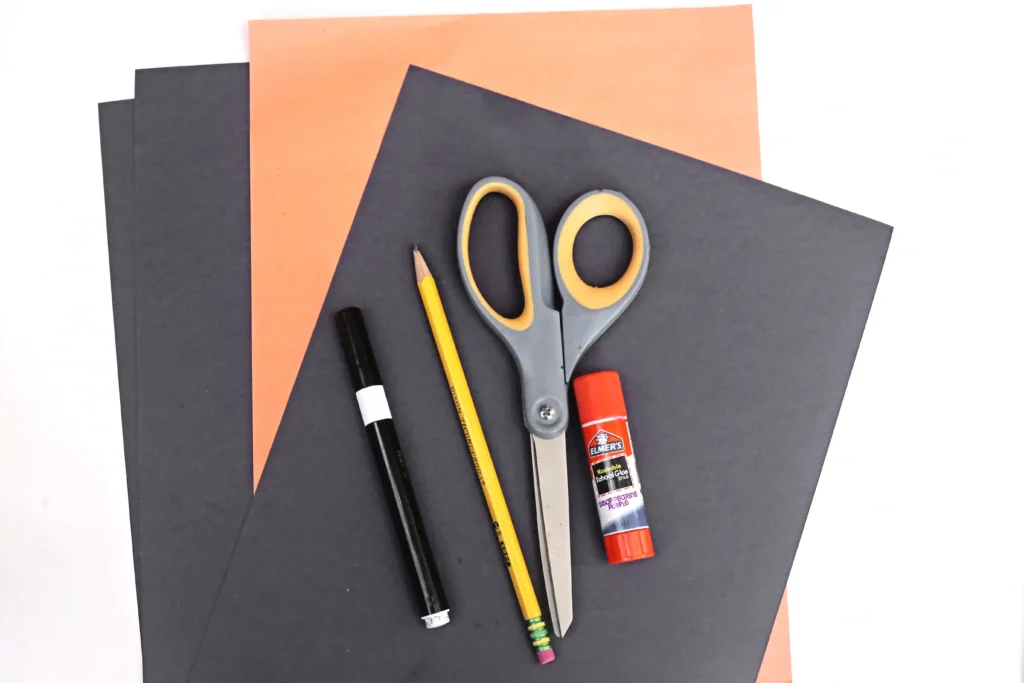 supplies for the spider headband: black and orange construction paper, black marker, pencil, scissors, and glue