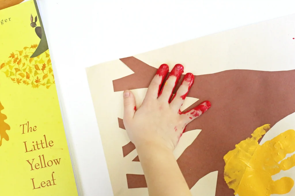 a child stamping his red painted hand on a brown construction paper tree 
