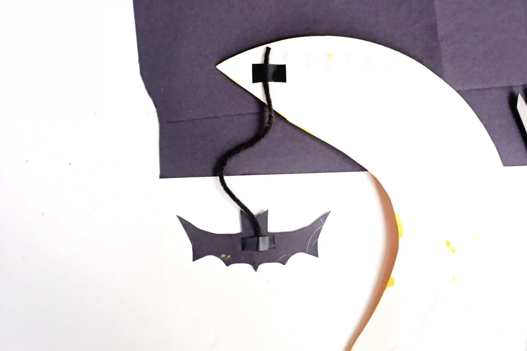 a construction paper bat with black string taped to the back of a paper plate