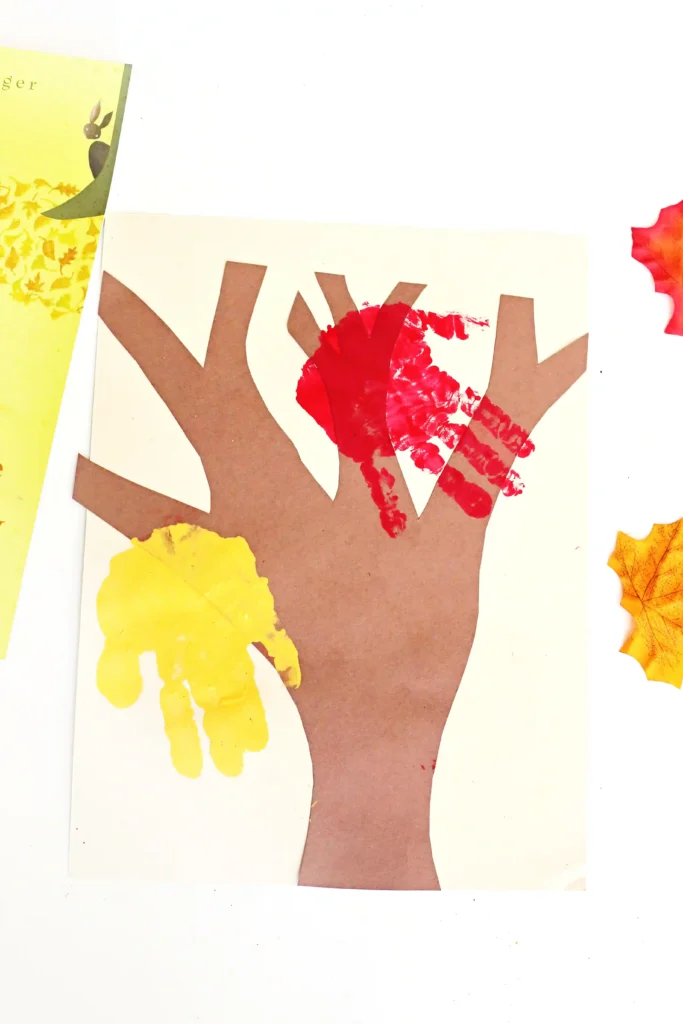 a tree cut out of construciton paper with red and yellow handprints to look like leaves