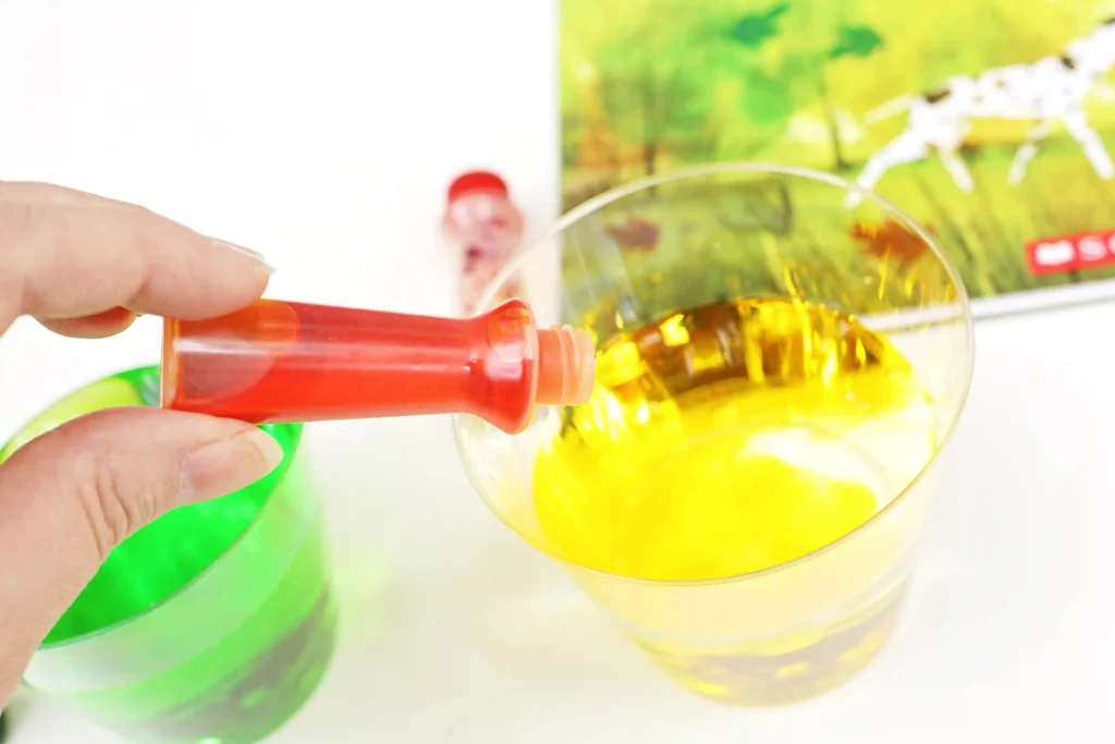 a hand adding yellow food coloring to a cup of water