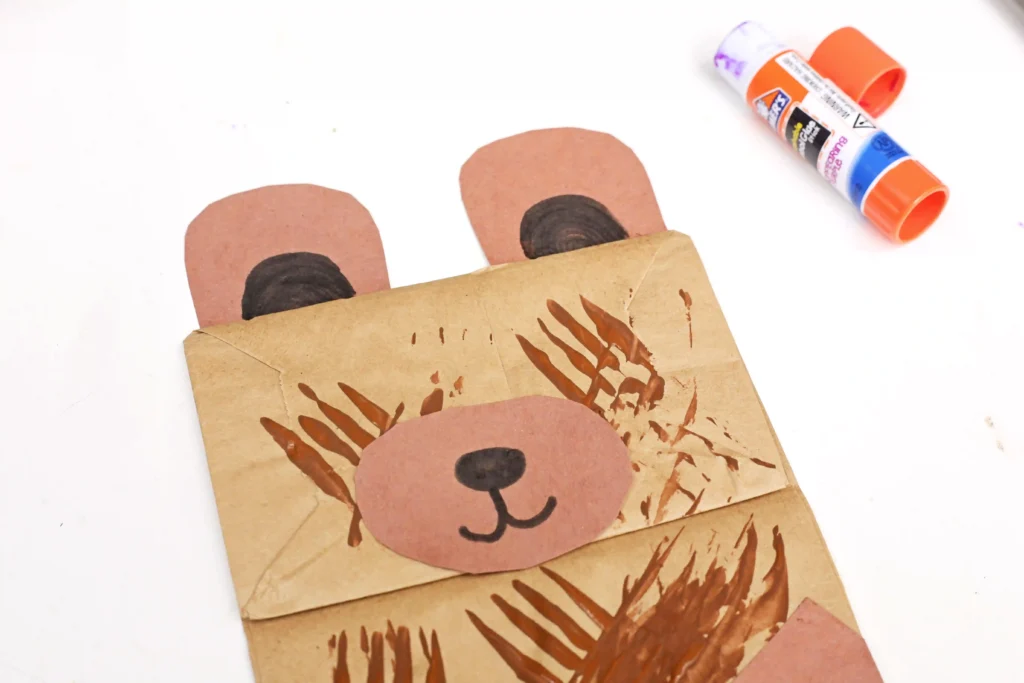 a paper bag with brown paint and bear snout, ears, and arms glued on