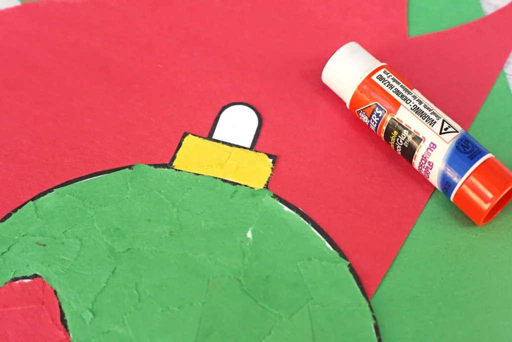 an ornament cut out of paper with red, green, and yellow torn construction paper glued on