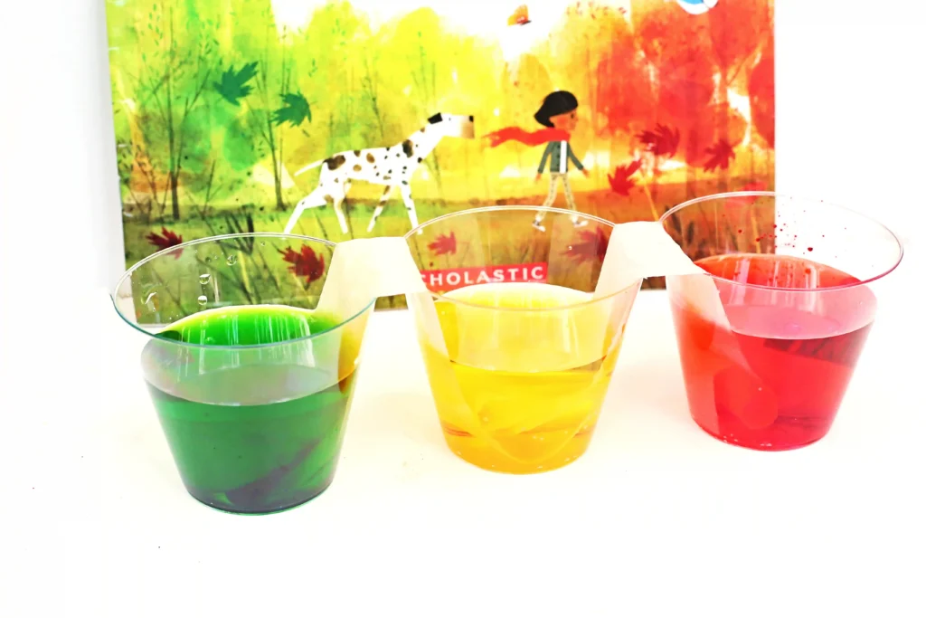 cups with red, green, and yellow water next to the book "goodbye summer, hello autumn"