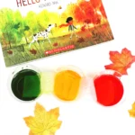 cups with red, green, and yellow water next to the book "goodbye summer, hello autumn"
