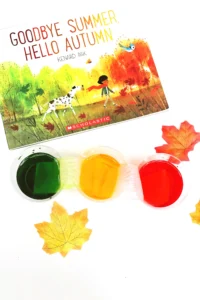cups with red, green, and yellow water next to the book "goodbye summer, hello autumn"