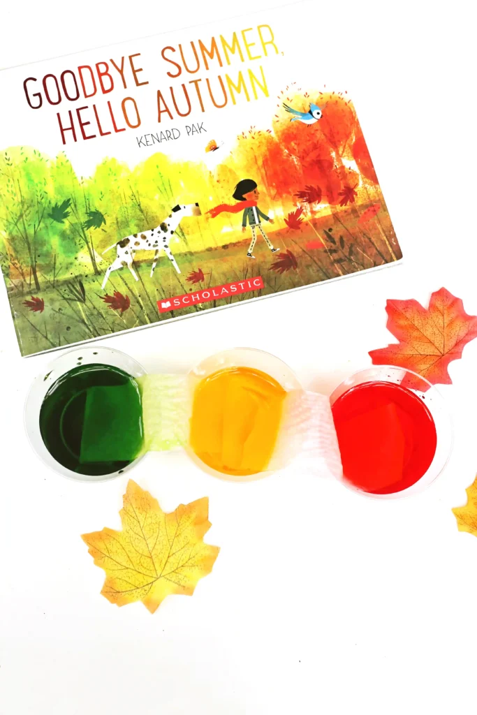 cups with red, green, and yellow water next to the book "goodbye summer, hello autumn"