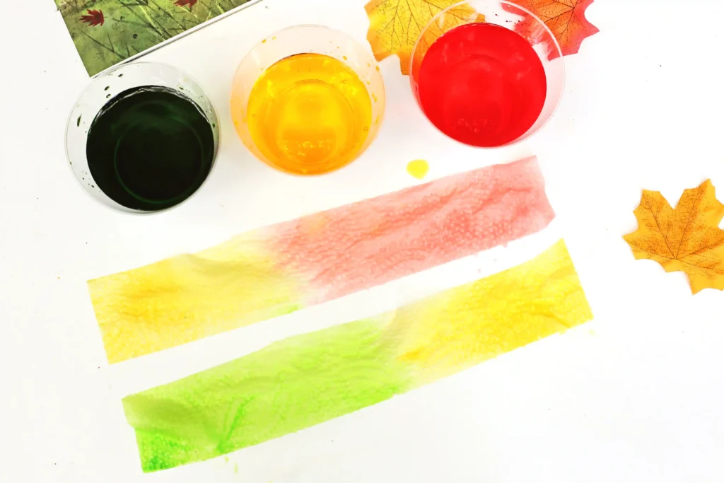 cups with red, green, and yellow water next to the book "goodbye summer, hello autumn" with colored paper towels