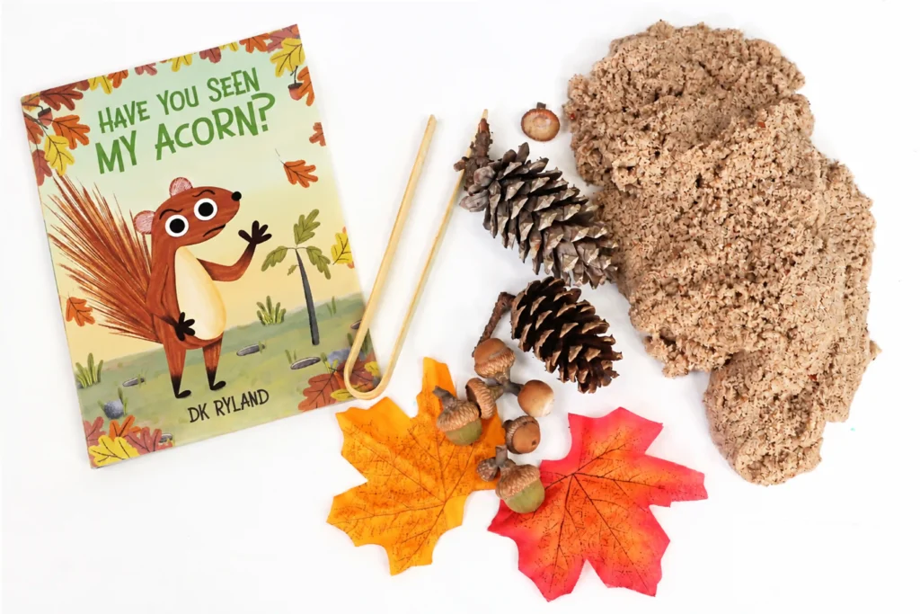 supplies for the have you seen my acorn sensory bin: sand, fake leaves, pinecones, and acorns