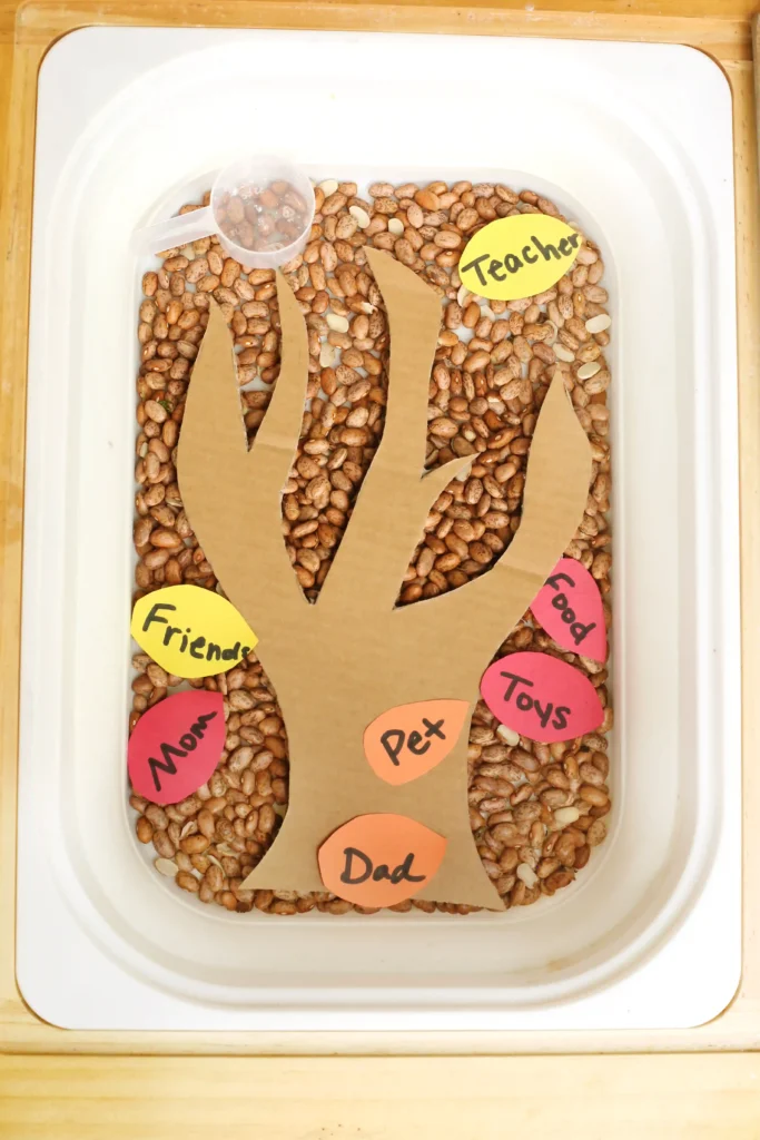 a thanksgiving sensory bin with dried beans, a cardboard tree, and construction paper feathers