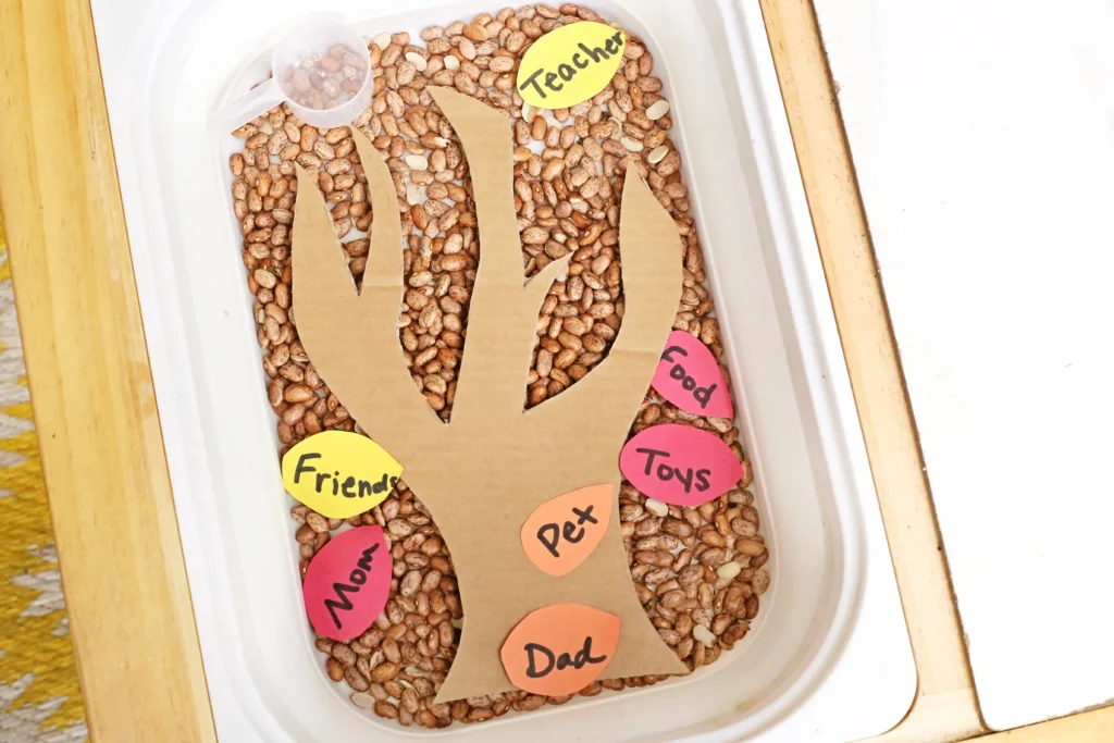 a thanksgiving sensory bin with dried beans, a cardboard tree, and construction paper feathers